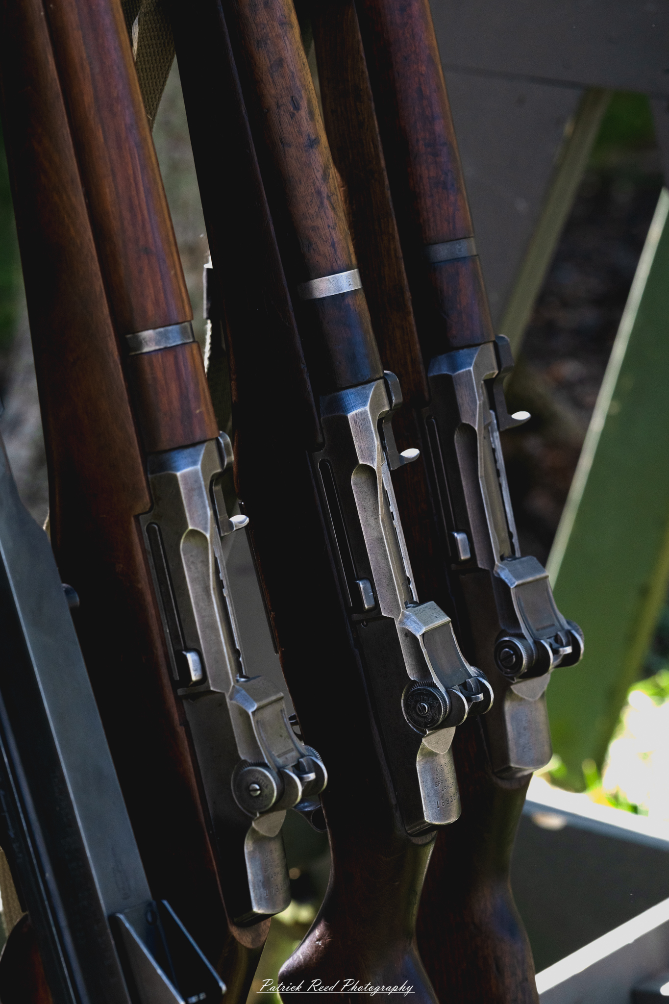 "Close-up shot of M1 Garand rifles arranged neatly, showcasing their distinct features and craftsmanship. The wooden stocks gleam with a rich finish, while the metal parts exhibit wear and patina, reflecting their history. Details such as the barrel, sight, and bolt mechanism are highlighted, emphasizing the rifle's engineering and reliability. The composition captures the essence of this iconic firearm, revered for its role in World War II and its lasting legacy in military history."